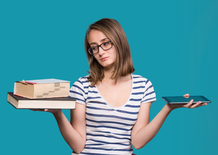 Pretty young girl  holding a book in one hand and a tablet-pc in the other on a blue background