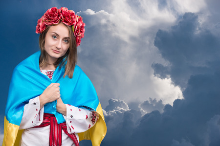 Portrait of attractive young girl in national dress with Ukrainian flag  against cloudy skyの写真素材
