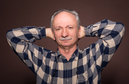 Elderly man with serious expression on a brown backgroundの写真素材