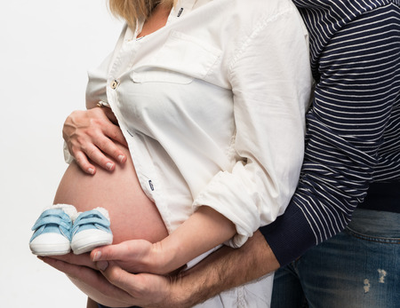 Newborn baby booties in parents hands, pregnant woman belly.の写真素材