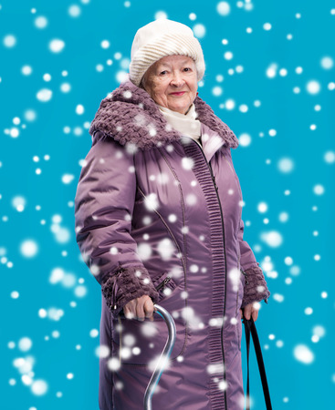 Portrait of smiling old woman in winter clothing standing with a caneの写真素材