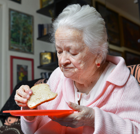 Old woman eating a slice of  bread at homeの写真素材