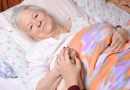 Caring hands holding old lady's hands in bed at hospitalの写真素材