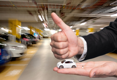 Closeup of businessman in black suit holding small car model and showing ok signの写真素材