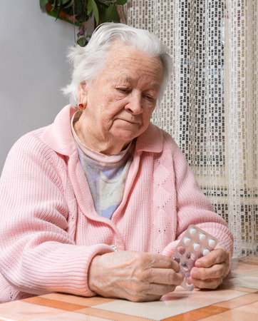 Old sad woman holding pills at homeの写真素材