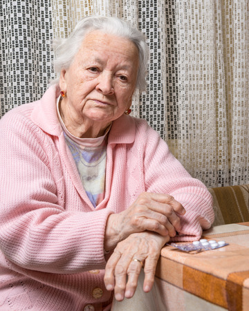 Old sad woman with pills at home.  Worried about  having to take too many pillsの写真素材