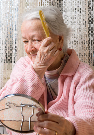 Portrait of old smiling woman combing her hair at homeの写真素材