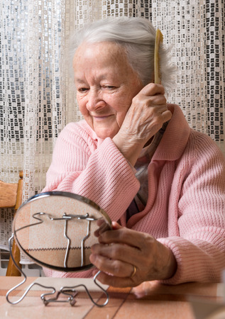 Portrait of old smiling woman combing her hair at homeの写真素材