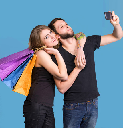 Happy couple with shopping bags taking selfie on a blue backgroundの写真素材