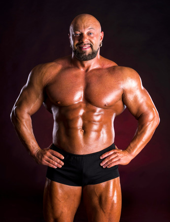 Handsome muscular bodybuilder posing on a dark red backgroundの写真素材