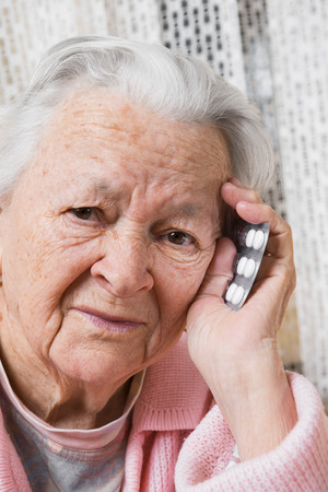 Old sad woman with pills at home. Worried about having to take too many pillsの写真素材