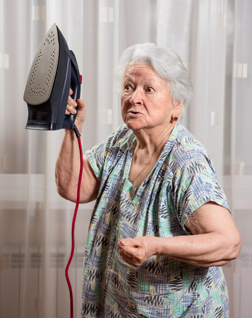 Angry old woman with an iron at homeの写真素材