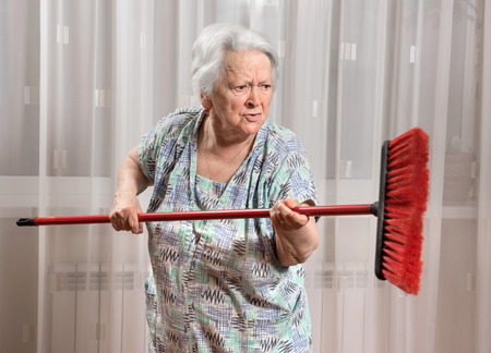 Old angry woman threatening with a broom at homeの写真素材
