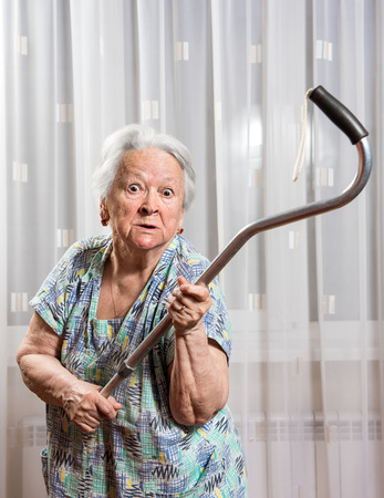 Old angry woman threatening with a cane at homeの写真素材