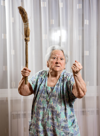 Old angry woman threatening with a broom at homeの写真素材