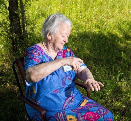 Old woman spraying insect repellent on skin outdoorの写真素材