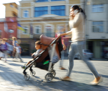 Mother with small child and a stroller walking down the street. Intentional motion blurの写真素材