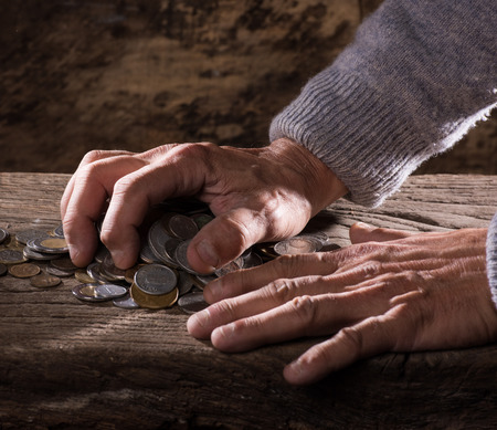 Close up of  caucasian old man's hands  and pile of old coins on a wooden backgroundの写真素材