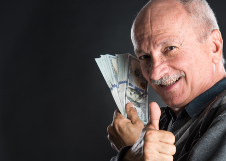 Happy elderly man showing dollars  on a dark background with copy-spaceの写真素材