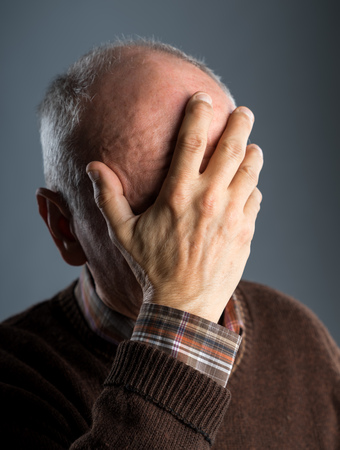 Elderly man suffering from a headache on a gray backgroundの写真素材
