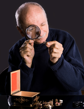 Senior jeweler  looking at jewelry through magnifying glass on a dark backgroundの写真素材