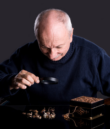 Senior jeweler  looking at jewelry through magnifying glass on a dark background