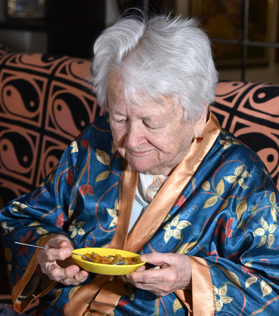 Portrait of old woman eating at homeの写真素材