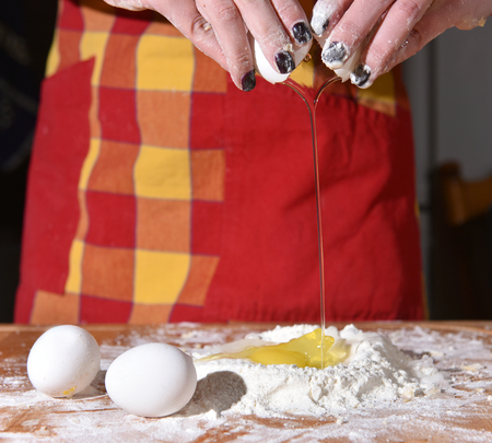 Woman breaking an egg into a heap of measured flour