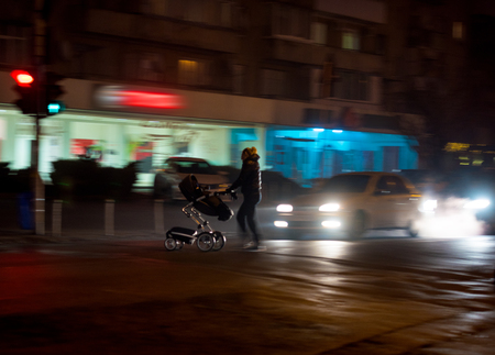 Woman with stroller on zebra crossing in the evening in motion blur