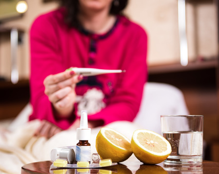 Sick woman lying in bed with high fever. Medicine on foregroundの写真素材