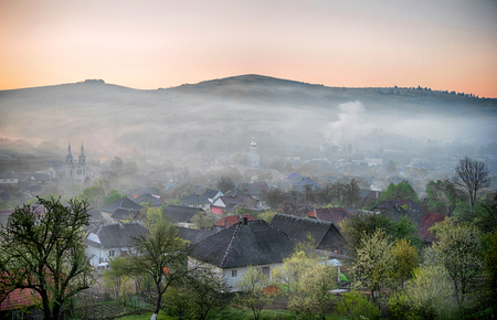 Spring landscape of scenic forest and small village. Smoking the gardens to avoid frostの写真素材
