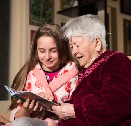 Grandmother and granddaughter reading a book at homeの写真素材