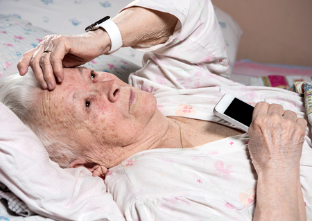 Old woman with smartwatch and smartphone  lying in bed at homeの写真素材