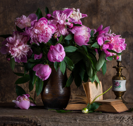 Artistic still life with peonies in vase and book on a wooden backgroundの写真素材