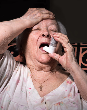 Old sick woman with asthma inhaler at homeの写真素材