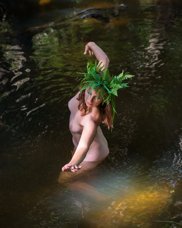 Romantic image of beautiful young nude woman with natural wreath enjoying summer time in the riverの写真素材