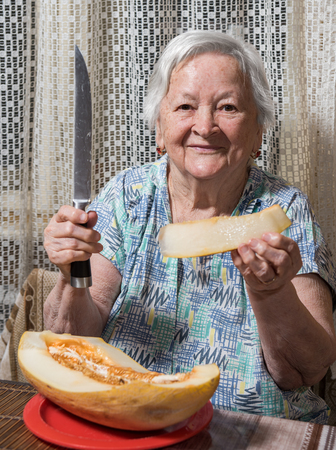 Portrait of senior woman eating yellow  melon at homeの写真素材