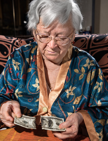Old woman looking at torn one hundred dollar bill at homeの写真素材