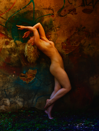 Young blonde nude woman standing beside an abandoned brick wall. Intentional colour shiftの写真素材