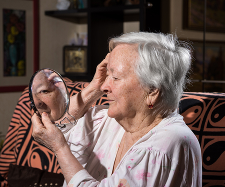 Portrait of old woman looking into a mirror at homeの写真素材