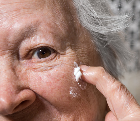 Old woman applying anti-aging cream at homeの写真素材