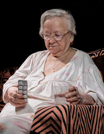 Old sick woman with pills and glass of water at homeの写真素材