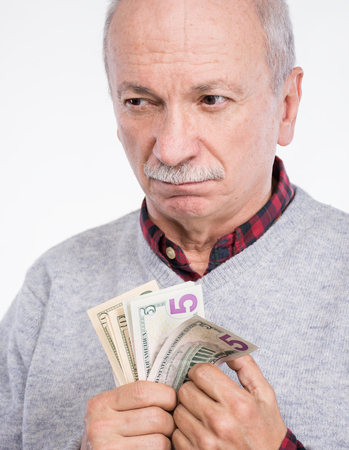Senior thoughtful man holding dollar bills on a white backgroundの写真素材