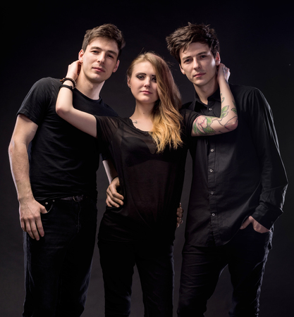 Love triangle. Young woman posing with two young man on a dark background in studioの写真素材