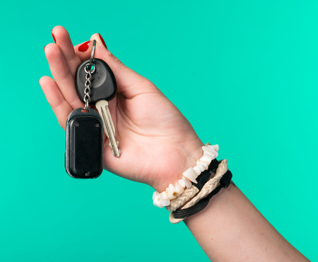 Close-up of woman hand holding car keys on a green background.Car selling or purchasing conceptの写真素材