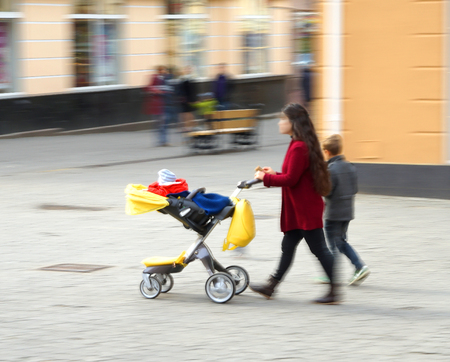 Young mother with small child in the stroller walking down the street. Intentional motion blur