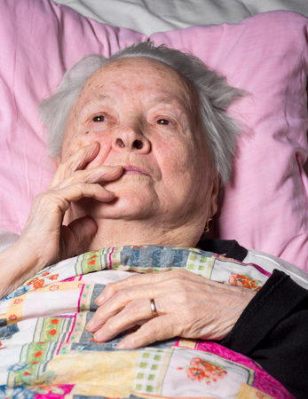 Old sick pensive woman lying at bedの写真素材