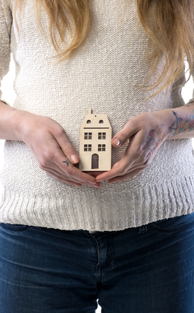 Pregnant woman holding wooden house. Close-up of womans handsの写真素材
