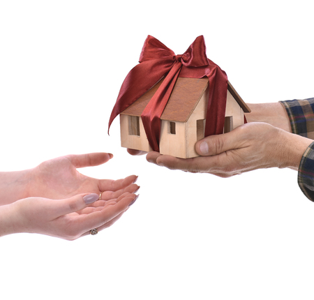 Close-up of man giving wooden house model tied with a bow to woman on a white background. Eco houseの写真素材