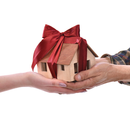 Close-up of man giving wooden house model tied with a bow to woman on a white background. Eco houseの写真素材